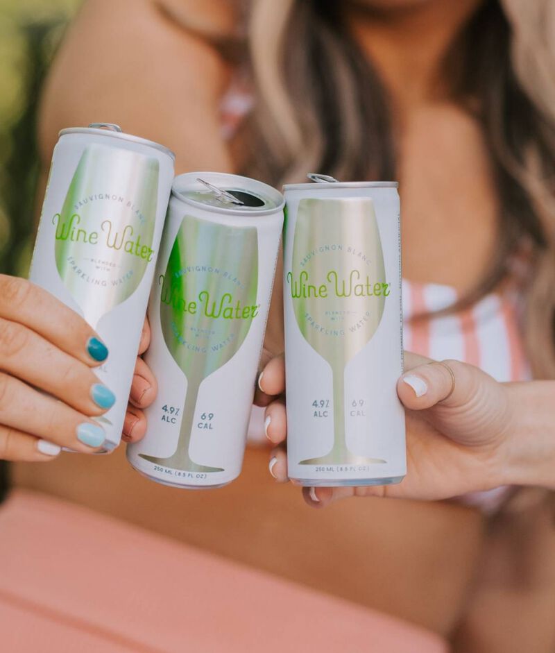 Three hands toasting with cans of Boutique Wine Water Sauvignon Blanc