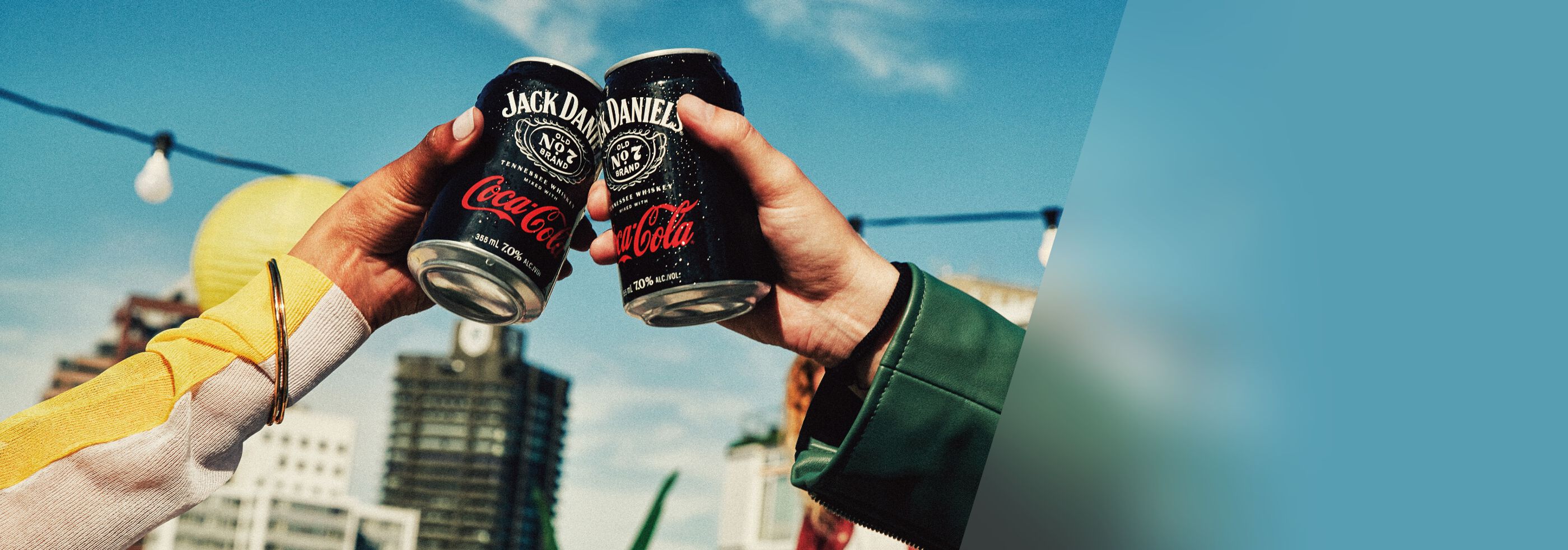 Two people toasting with cans of Jack Daniel’s & Coca-Cola Ready to Drink with a city background